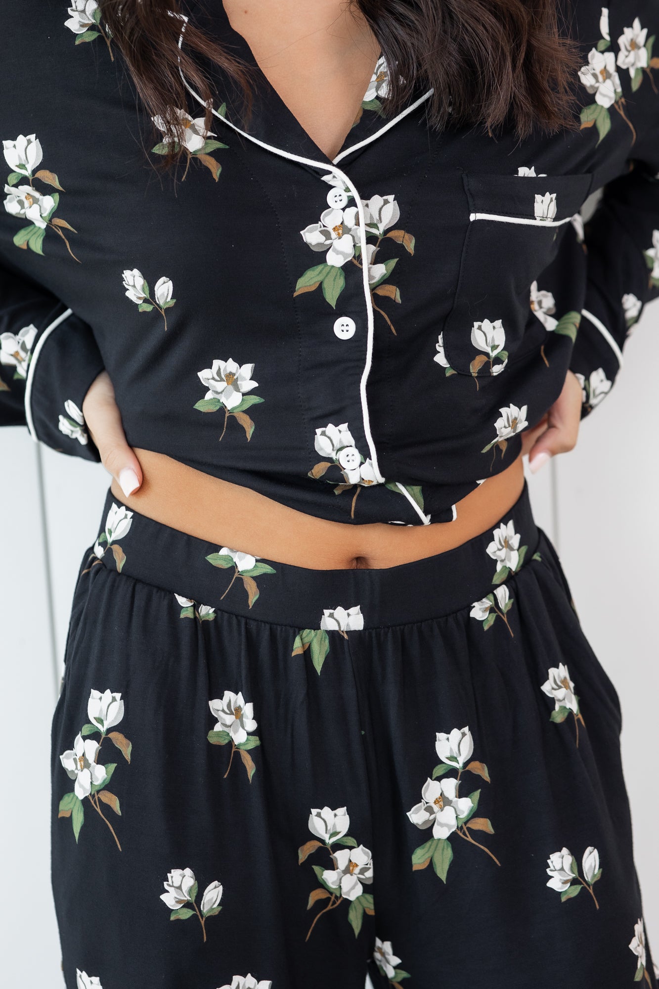 Woman modeling black long sleeve button up pajamas in a magnolia print showing waistband 