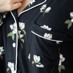 Woman modeling black long sleeve button up pajamas in a magnolia print showing collar and shirt pocket