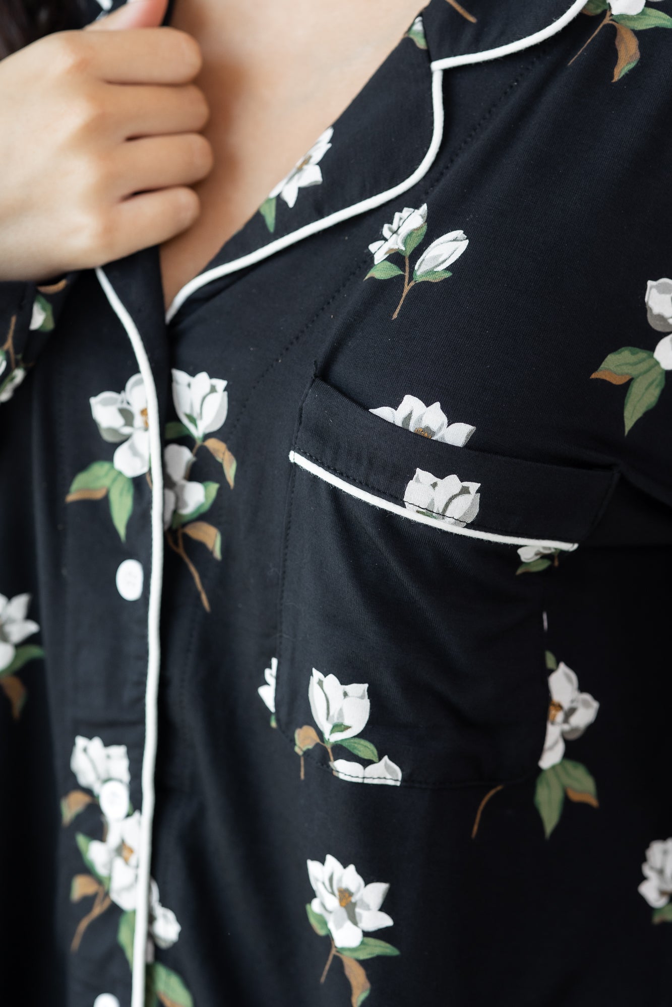 Woman modeling black long sleeve button up pajamas in a magnolia print showing collar and shirt pocket