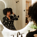 Woman looking in a mirror wearing Magnolia printed black robe in a neutral bathroom 