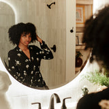 Woman looking in a mirror wearing Magnolia printed black robe in a neutral bathroom 