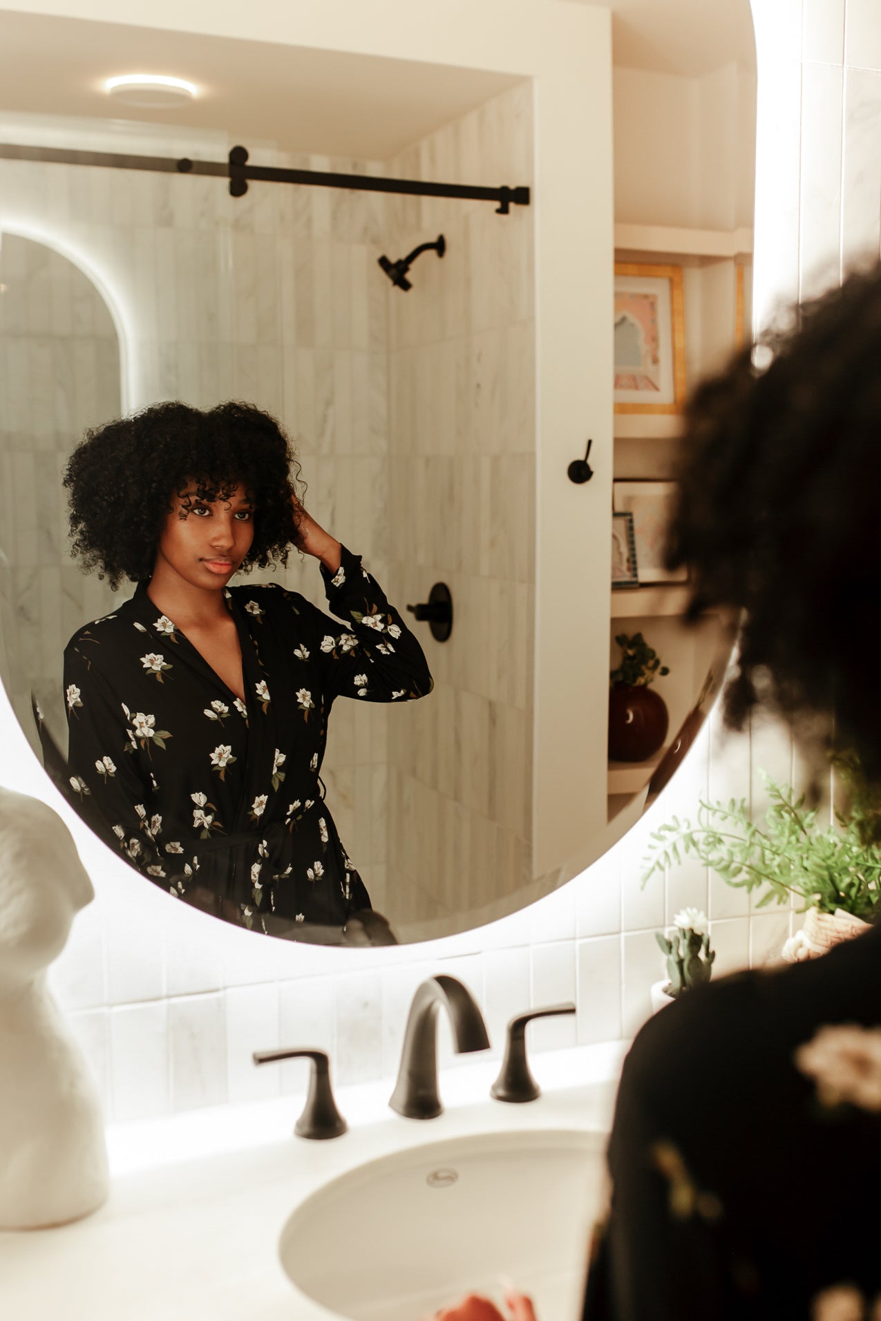 Woman looking in a mirror wearing Magnolia printed black robe in a neutral bathroom 