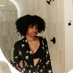 Woman looking in a mirror wearing Magnolia printed black robe in a neutral bathroom 