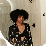 Woman looking in a mirror wearing Magnolia printed black robe in a neutral bathroom 