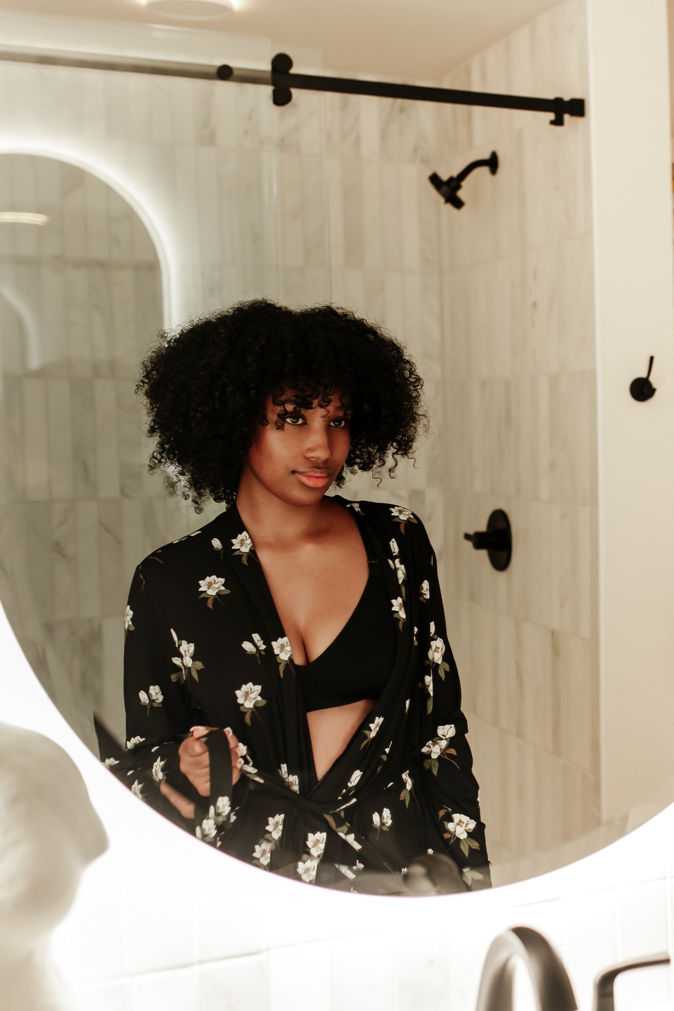 Woman looking in a mirror wearing Magnolia printed black robe in a neutral bathroom 
