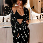 Woman wearing Magnolia printed black robe and black bra in a neutral bathroom 