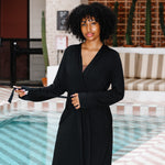 Woman in a black robe standing by a poolside with a striped awning above.