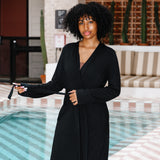 Woman in a black robe standing by a poolside with a striped awning above.