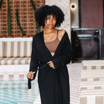 Woman in a black robe standing by a poolside with a striped umbrella in the background
