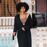 Woman in a black robe standing by a poolside with a striped umbrella in the background