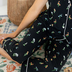 Model sitting on floor wearing Women's Short Sleeve Cropped Pajama Set in Midnight Wildflower print with a pot in the background 