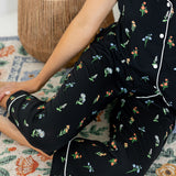 Model sitting on floor wearing Women's Short Sleeve Cropped Pajama Set in Midnight Wildflower print with a pot in the background 
