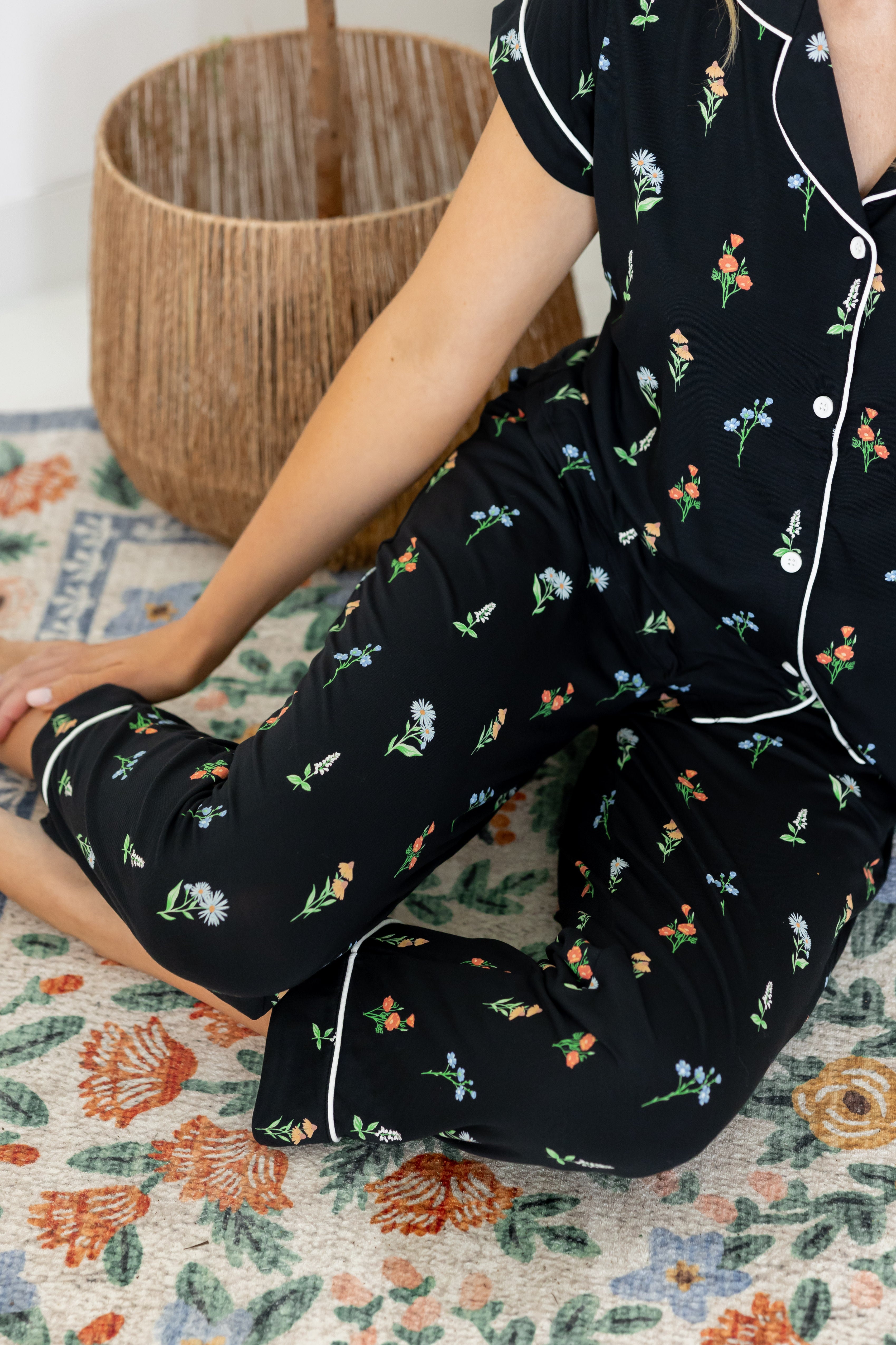 Model sitting on floor wearing Women's Short Sleeve Cropped Pajama Set in Midnight Wildflower print with a pot in the background 