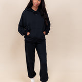 Woman wearing Women's Jogger Pants in Midnight color and a similar color Hoodie on a beige background