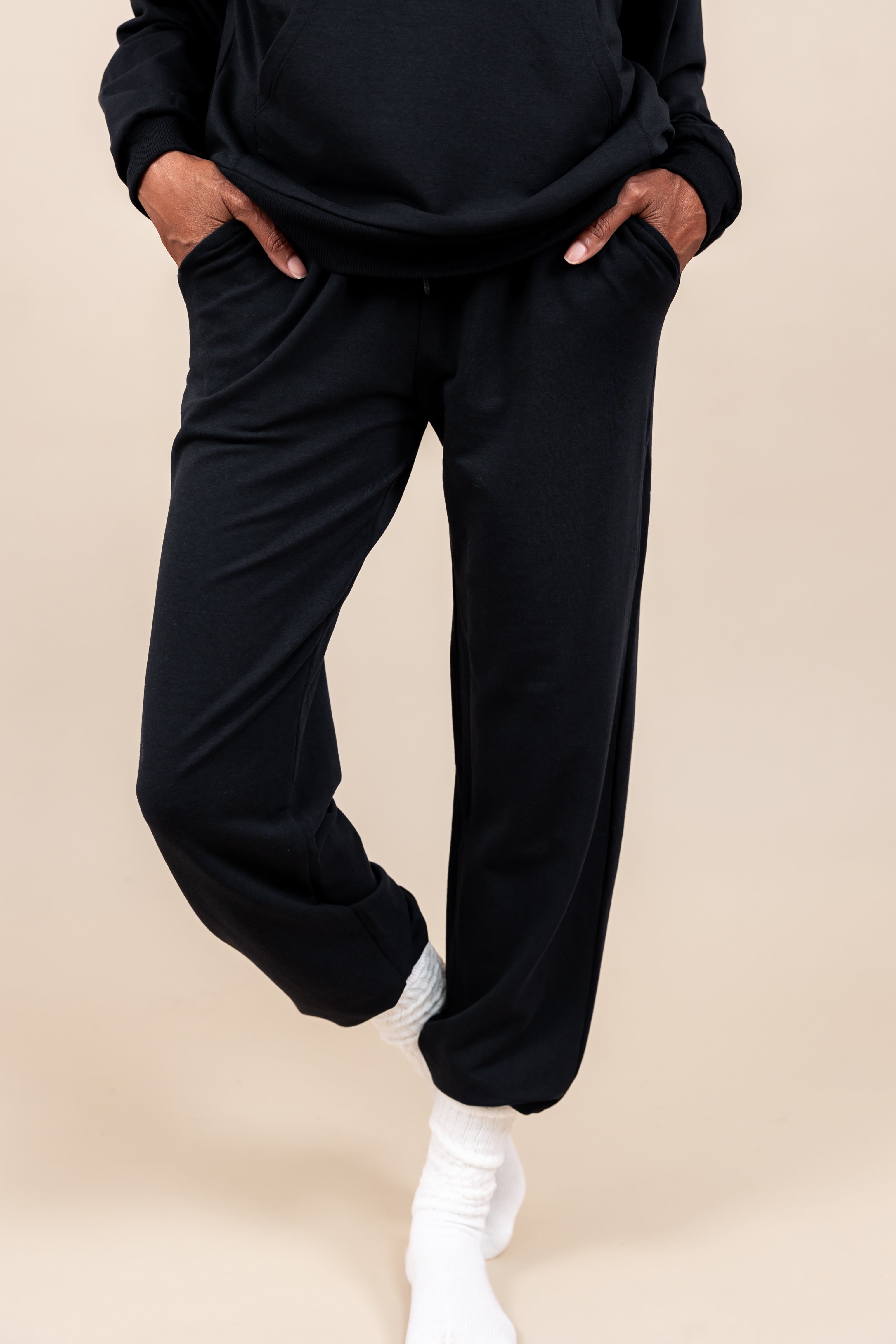 Woman wearing Women's Jogger Pants in Midnight color with pockets under a similar color Hoodie on a beige background