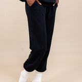Side view of Woman wearing Women's Jogger Pants in Midnight color with pockets under a similar color Hoodie on a beige background