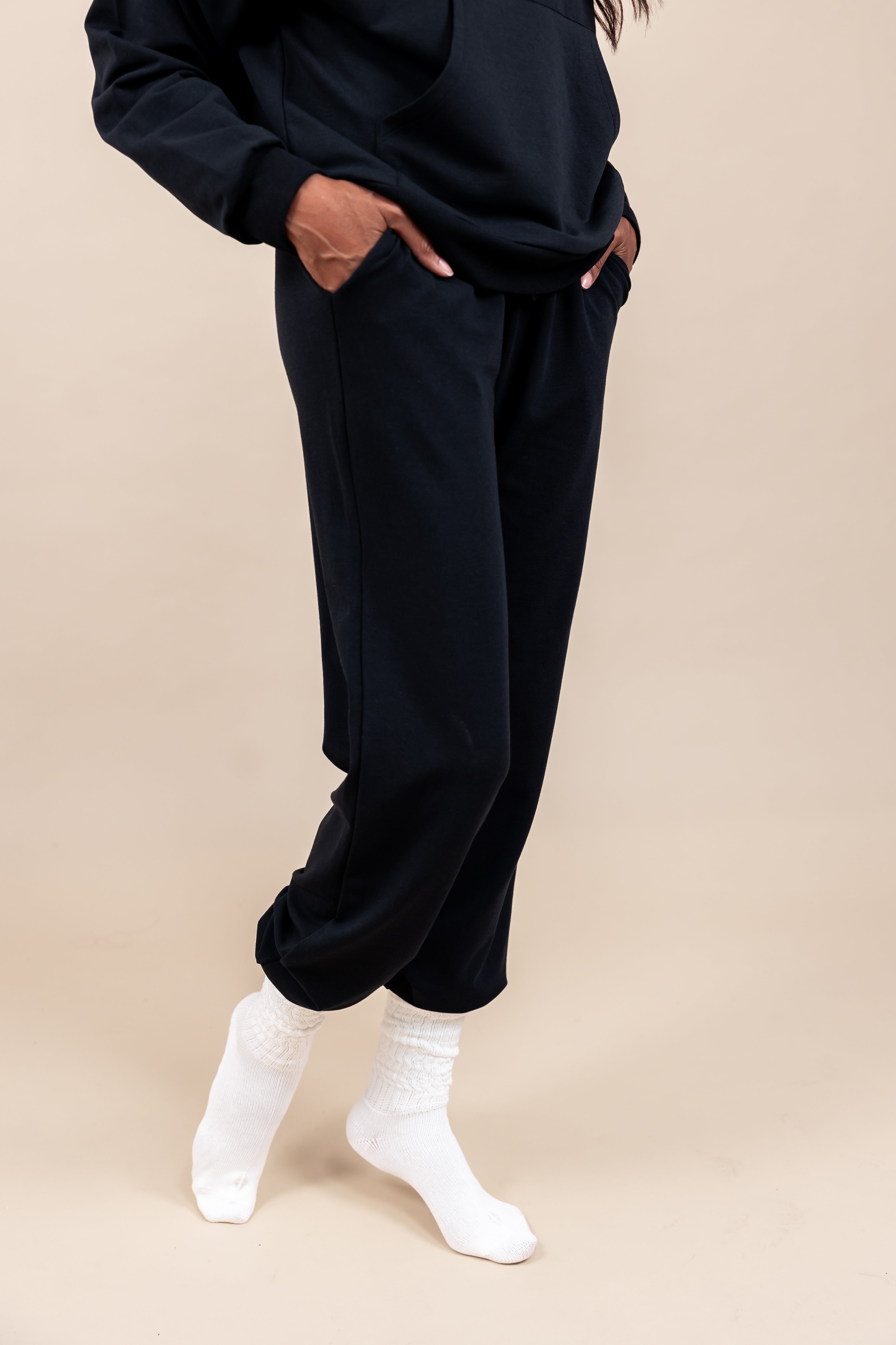 Side view of Woman wearing Women's Jogger Pants in Midnight color with pockets under a similar color Hoodie on a beige background