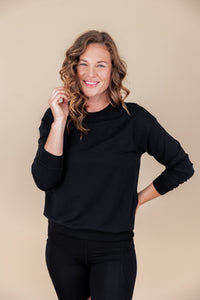Woman smiling with one hand to her hair and the other hand on her hip wearing a sweatshirt in midnight and black biker shorts