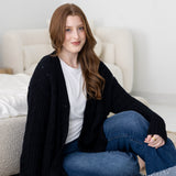 Woman sitting in a neutral bedroom wearing a black cardigan, white tee and jeans  ::: Model is 5'7" wearing size M ///
