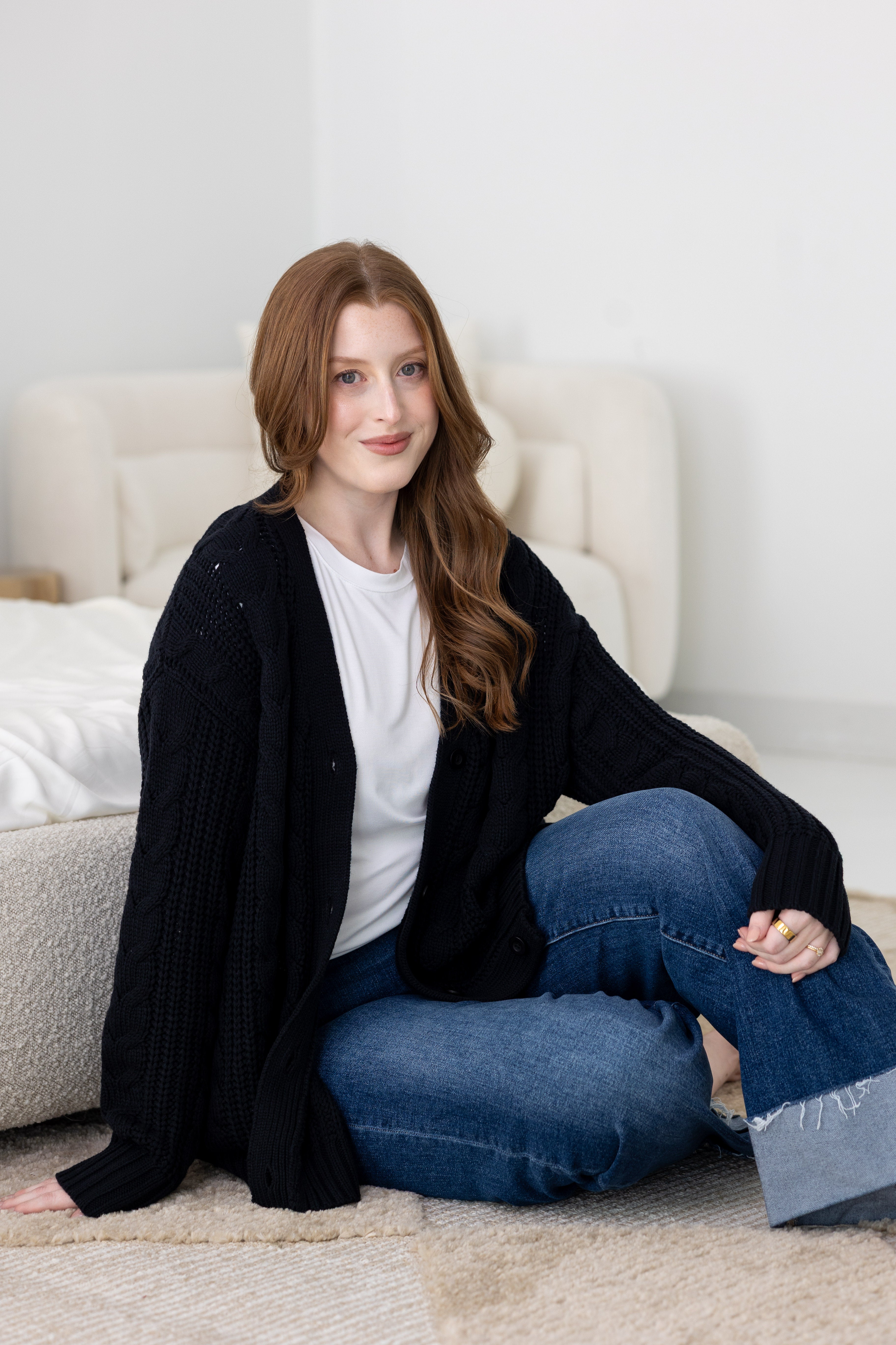 Woman sitting in a neutral bedroom wearing a black cardigan, white tee and jeans  ::: Model is 5'7" wearing size M ///