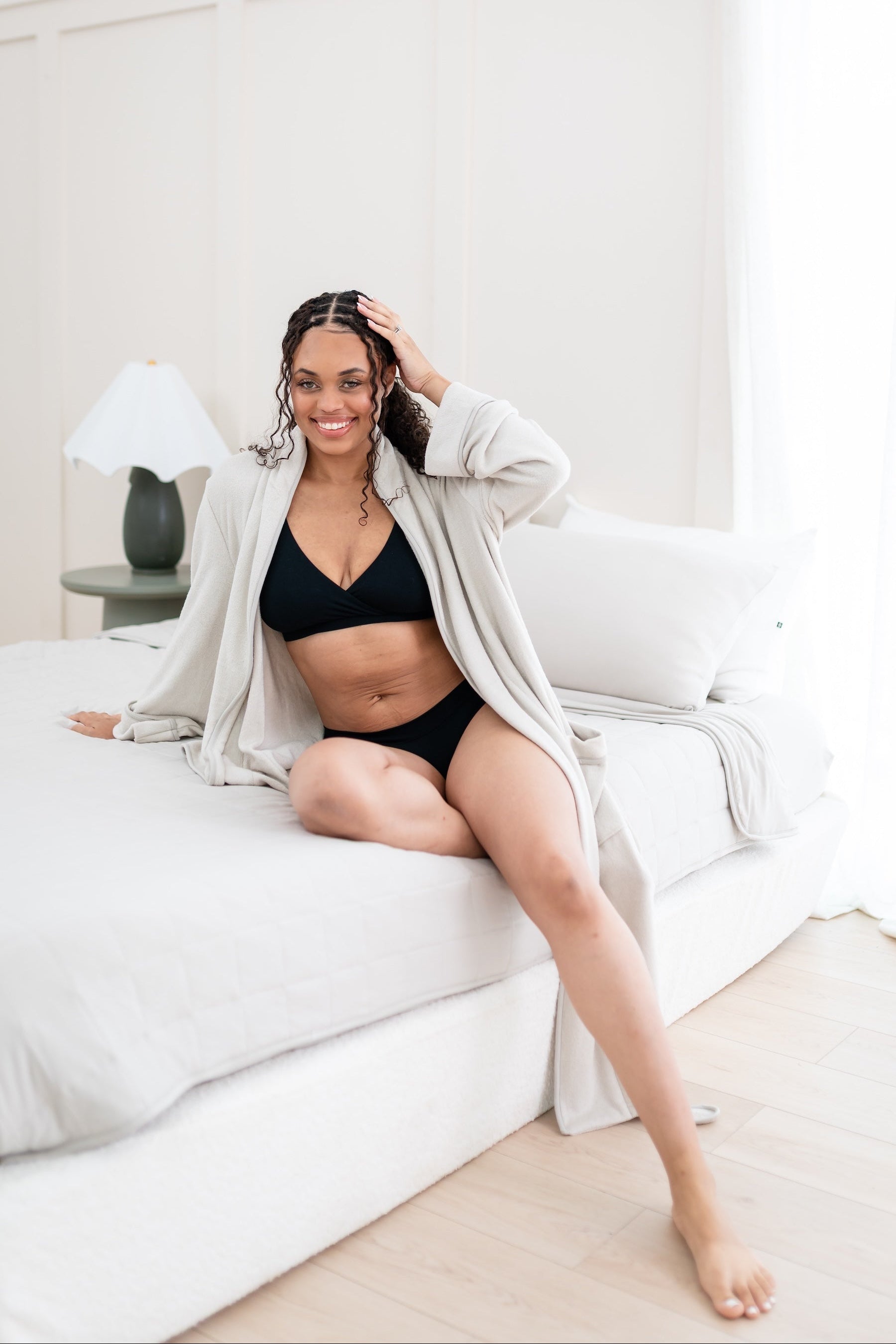 Woman in black intimates set and oat robe sitting on a bed.
