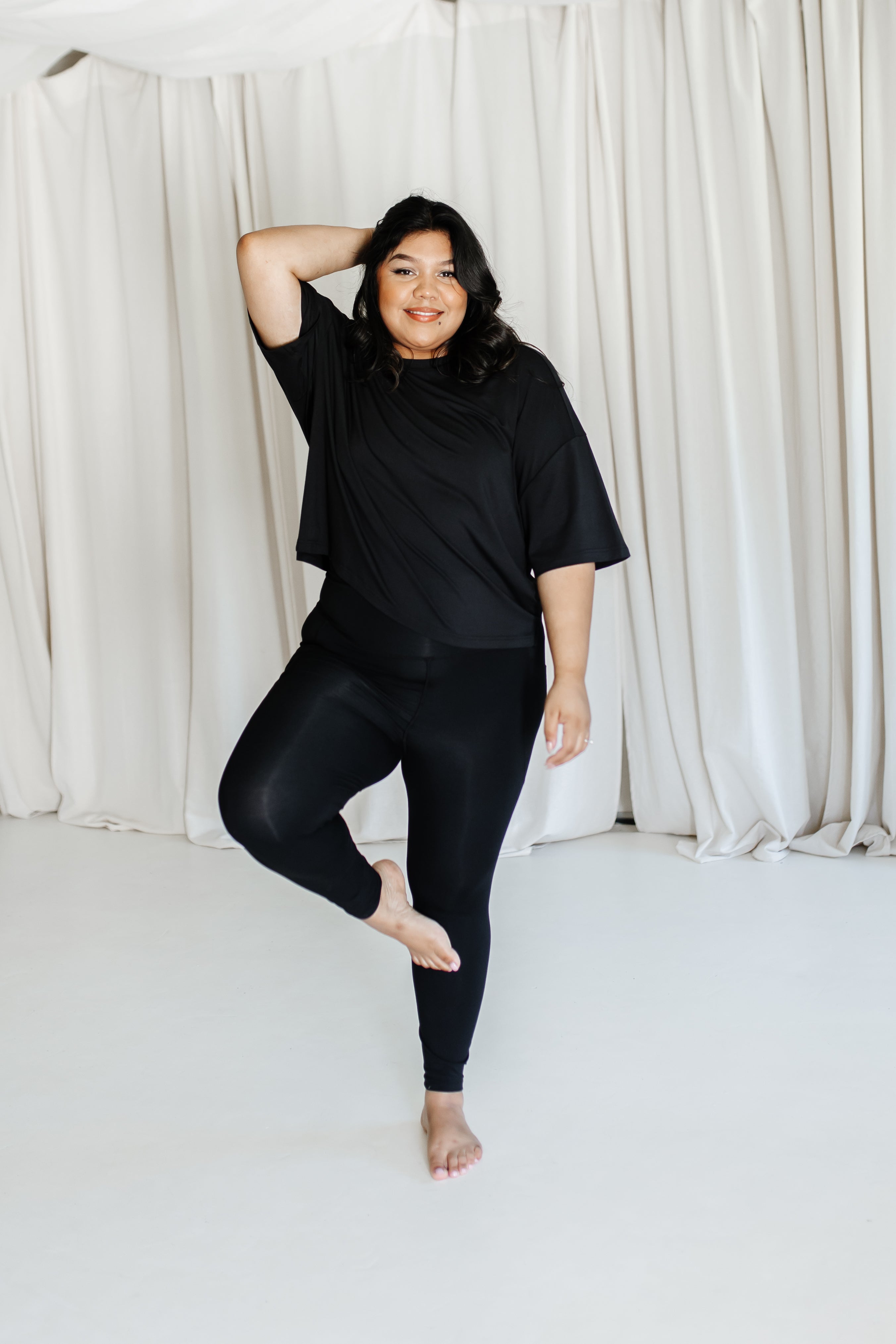 Female standing on one leg wearing the Bamboo Flex Women’s Leggings in Midnight and short sleeve tee