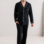 Male model standing in a white room while wearing the Kyte Men's Long Sleeve Pajama Set in Midnight
