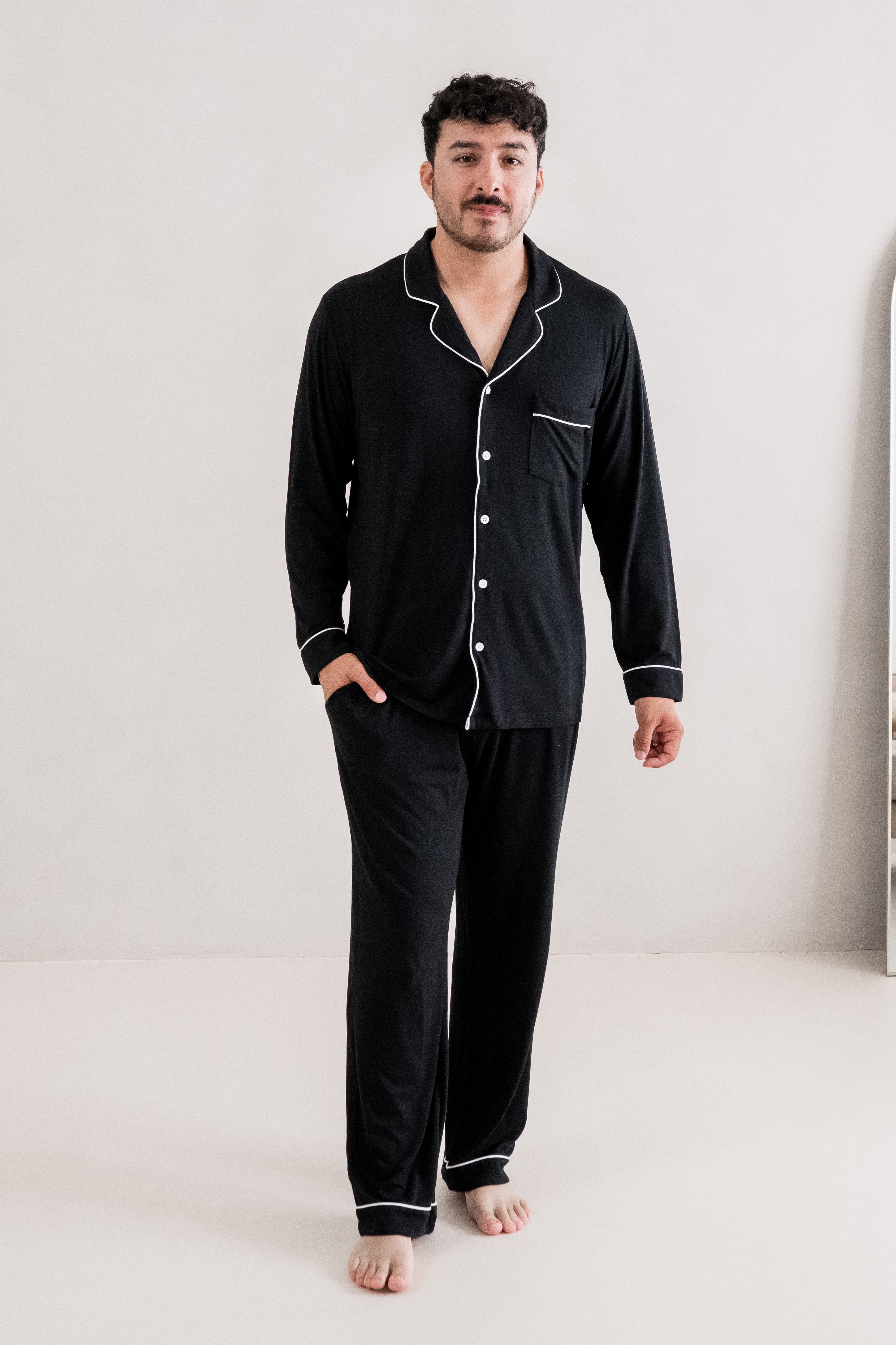 Male model standing in a white room while wearing the Kyte Men's Long Sleeve Pajama Set in Midnight