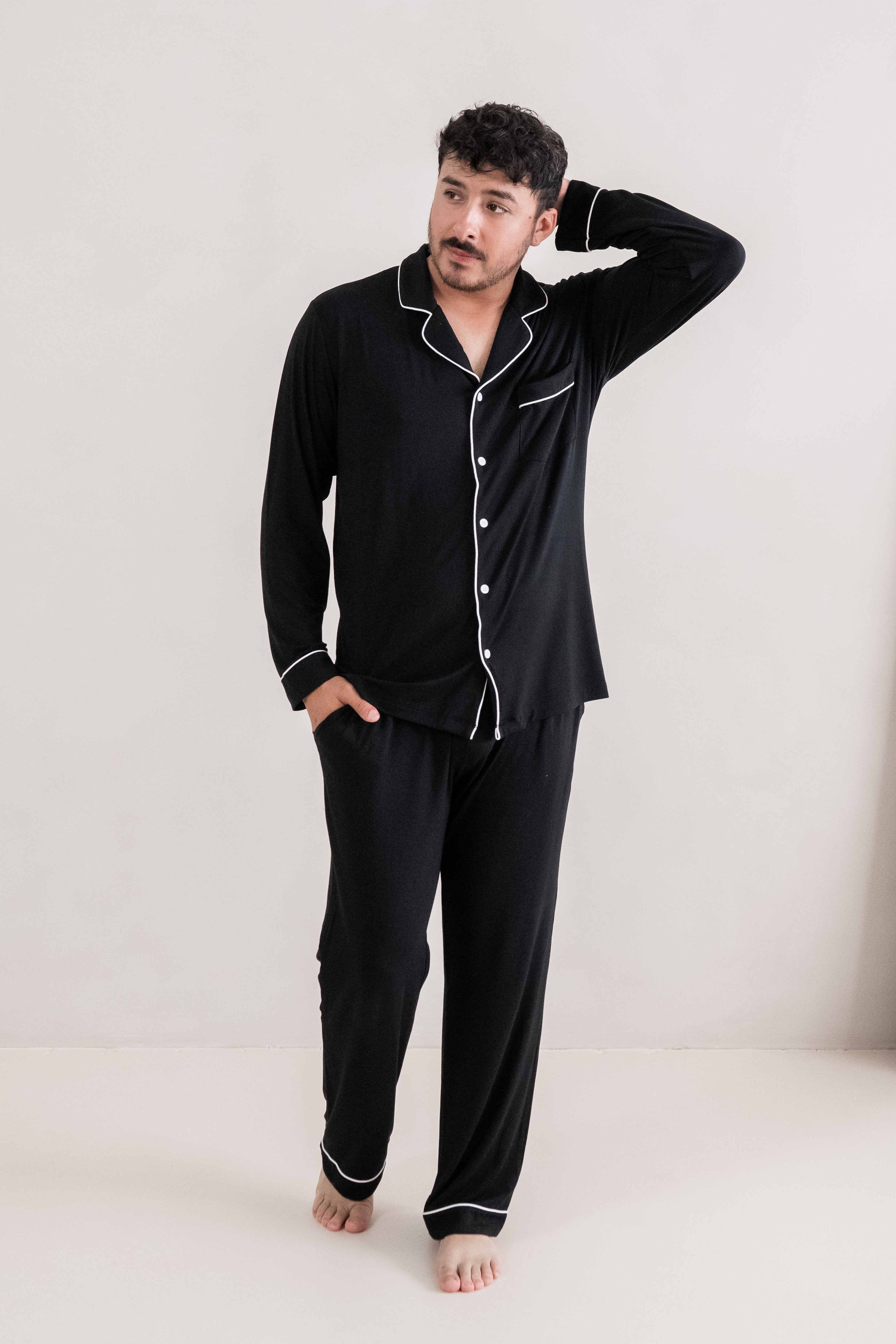 Man standing with one hand on his head while modeling the Kyte Men's Long Sleeve Pajama Set in Midnight