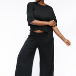 Female model standing in front of a white background wearing the Women's Wide Leg Pant in Midnight with matching women's short sleeve tee