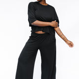 Female model standing in front of a white background wearing the Women's Wide Leg Pant in Midnight with matching women's short sleeve tee