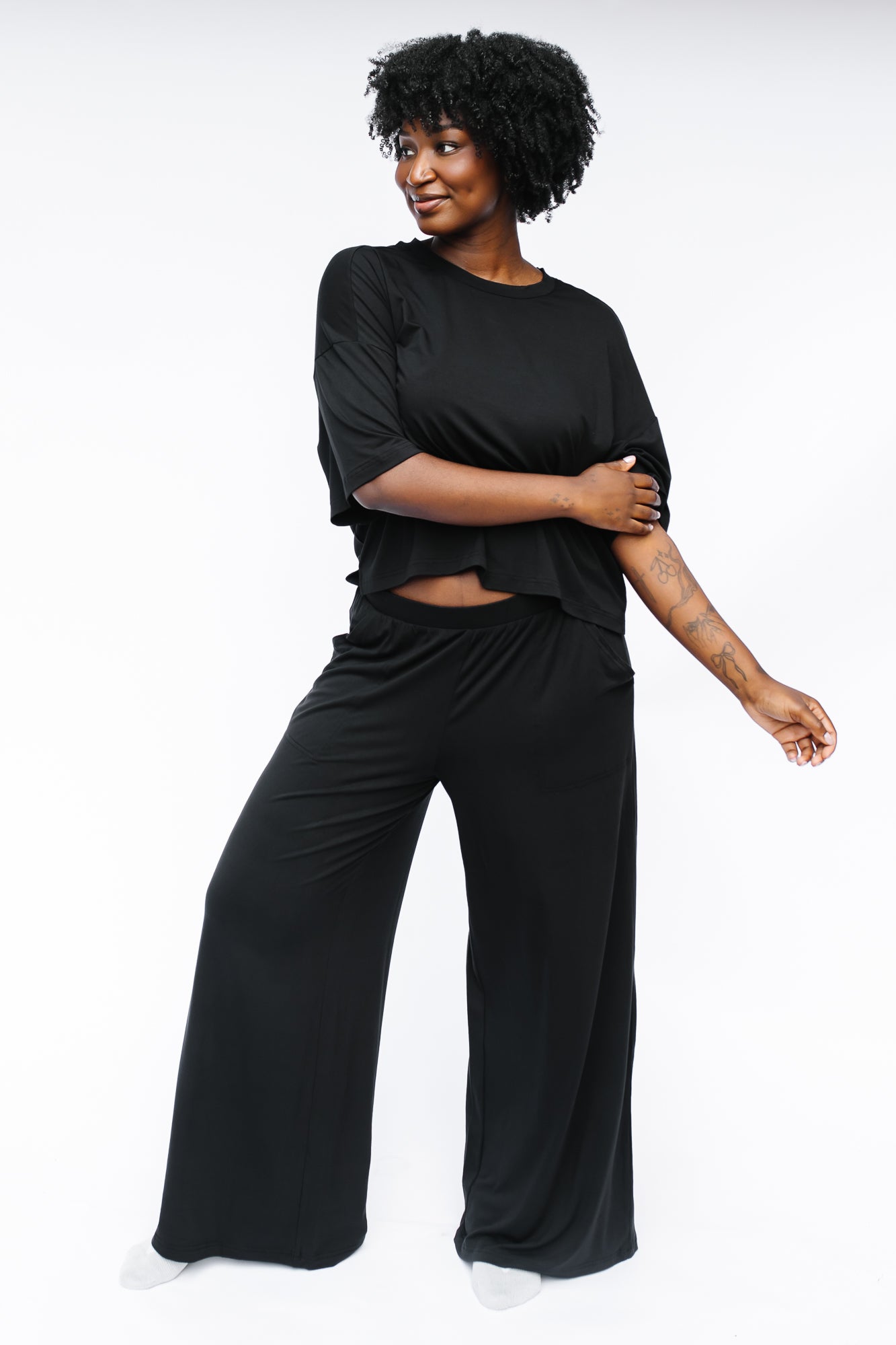 Female model standing in front of a white background wearing the Women's Wide Leg Pant in Midnight with matching women's short sleeve tee
