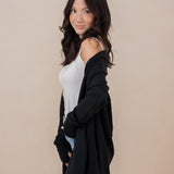 Woman standing sideways with one hand in her pocket, wearing the Kyte Women's French Terry Wrap Top in Midnight paired with jeans 
