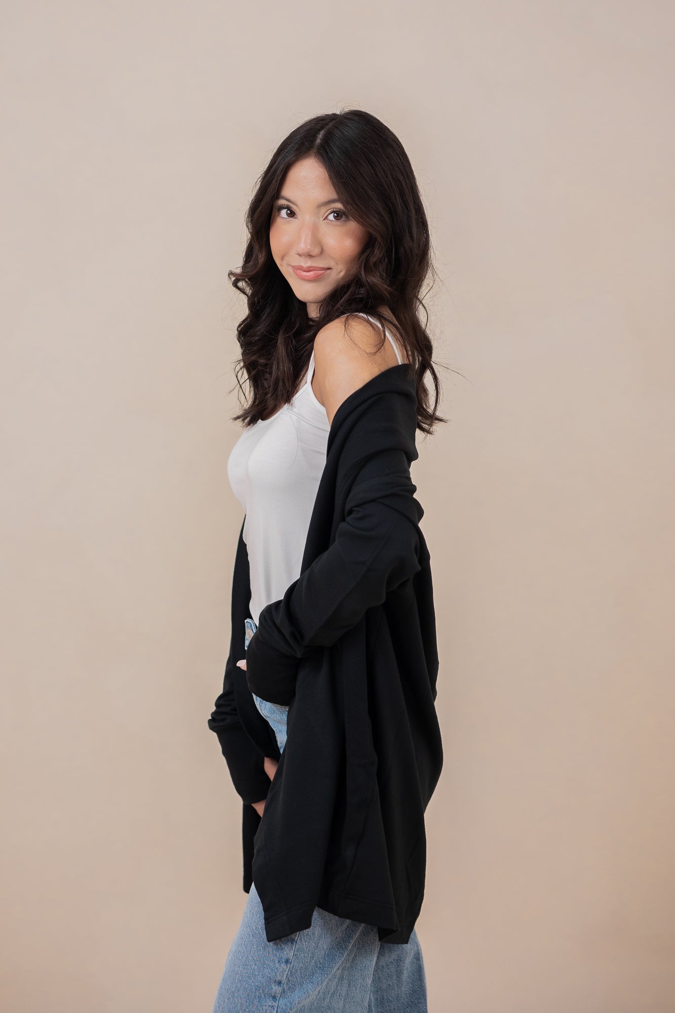 Woman standing sideways with one hand in her pocket, wearing the Kyte Women's French Terry Wrap Top in Midnight paired with jeans 