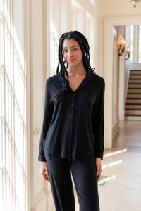 Woman soft smiling against a window wearing a long sleeve pajama set in midnight