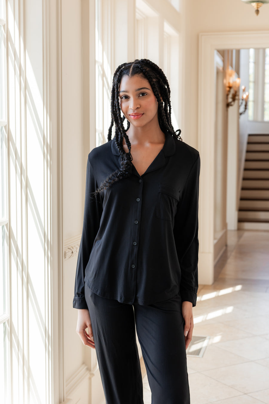 Woman soft smiling against a window wearing a long sleeve pajama set in midnight