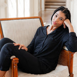 Woman wearing black button up pajamas lounging on a chair in an elevated room
---PJ 4