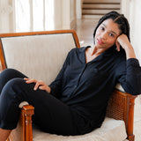 Woman wearing black button up pajamas lounging on a chair in an elevated room
---PJ 4