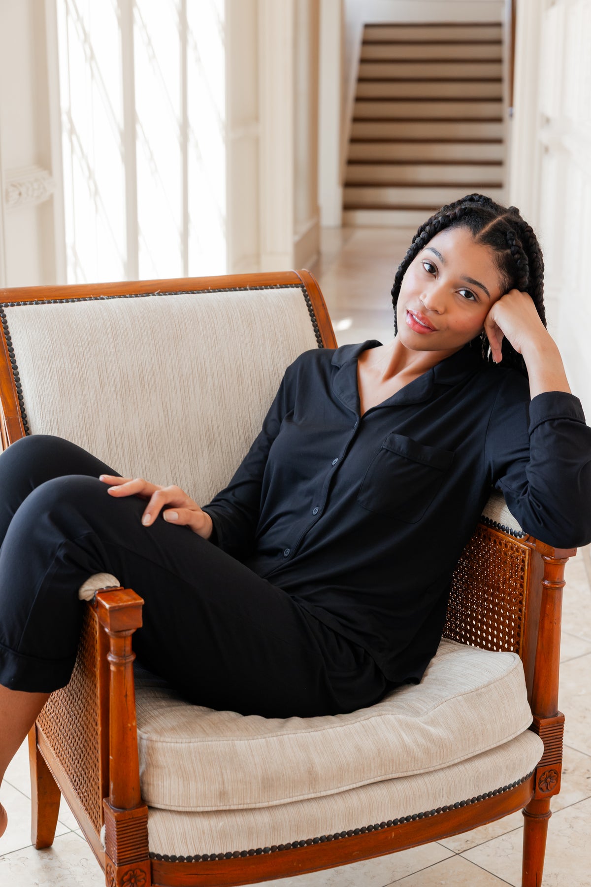 Woman wearing black button up pajamas lounging on a chair in an elevated room
---PJ 4