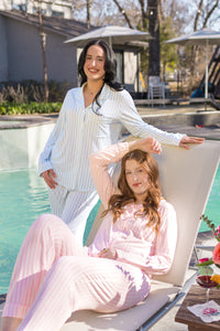 Two women in light colored striped pajamas by a poolside with umbrellas in the background