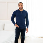 Man modeling Men's Long Sleeve Henley Top in Navy with jeans with hand in pocket with a bedroom backdrop