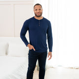 Man modeling Men's Long Sleeve Henley Top in Navy with jeans with hand in pocket with a bedroom backdrop