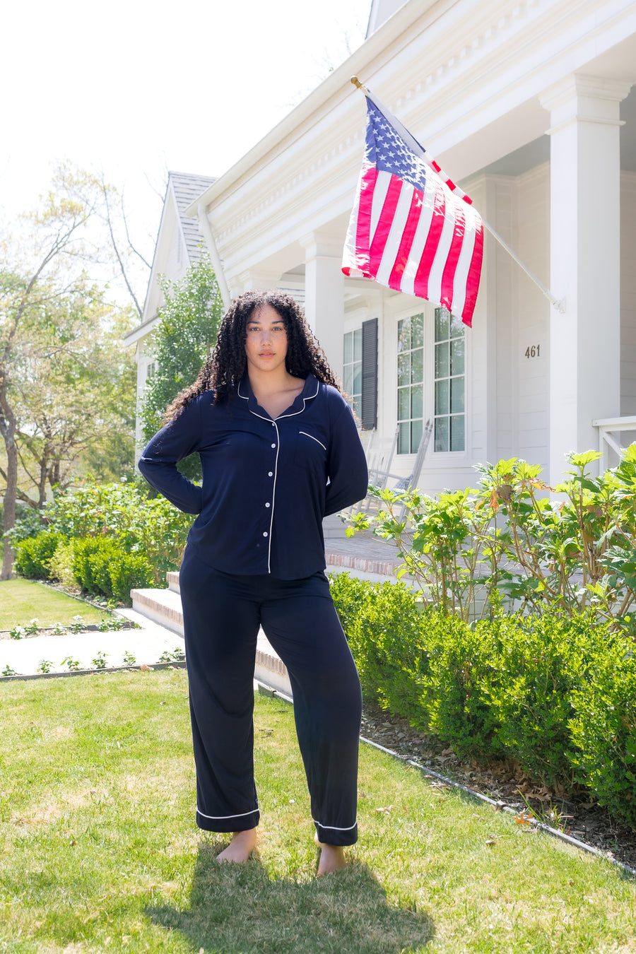 Woman in navy pajamas standing in front of a house with an American flag.