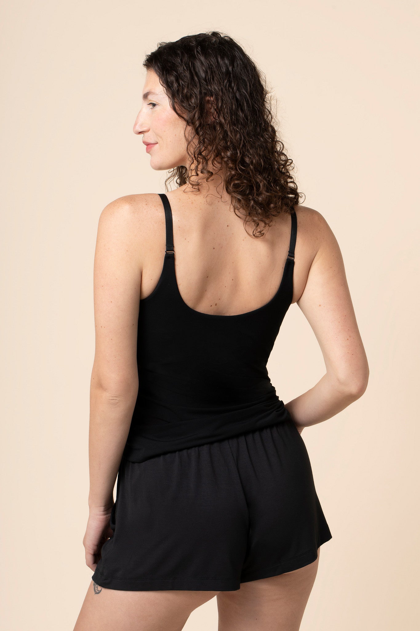 Model showcasing the back side and straps on the Women's Nursing Tank in Midnight in front of a beige back ground 