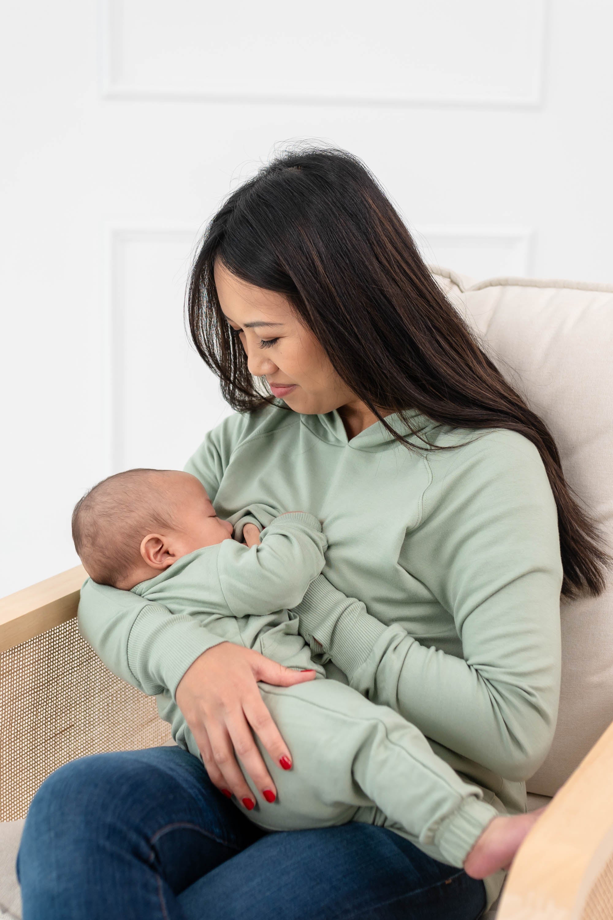 Woman breastfeeding infant while wearing the Women's French Terry Nursing Hoodie in Thyme