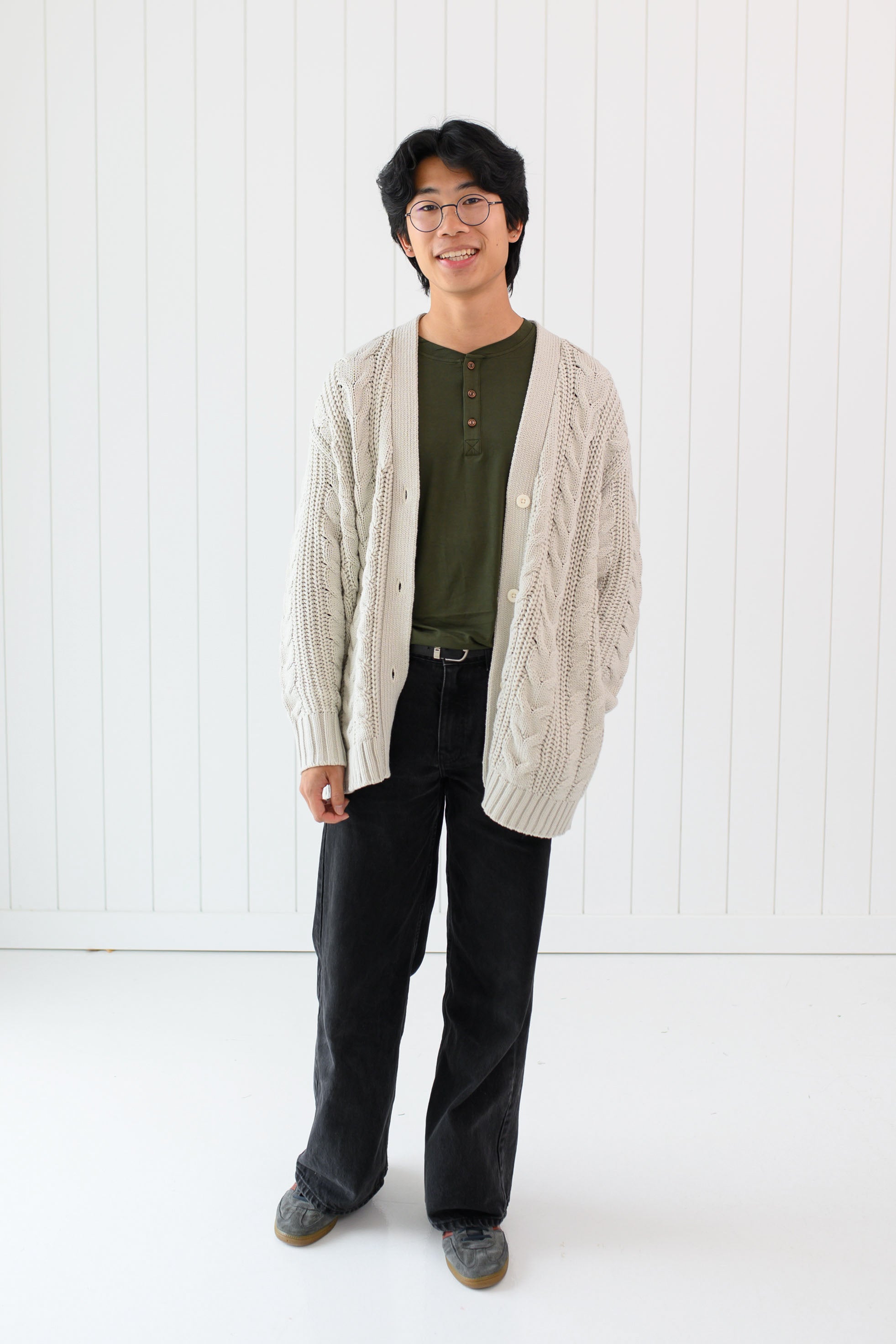 Man standing in a white room while modeling the Chunky Cable Knit Cardigan in Oat