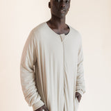 A man wearing a long-sleeved, beige sleep sack with a split neckline and side pockets, standing against a solid light beige background.