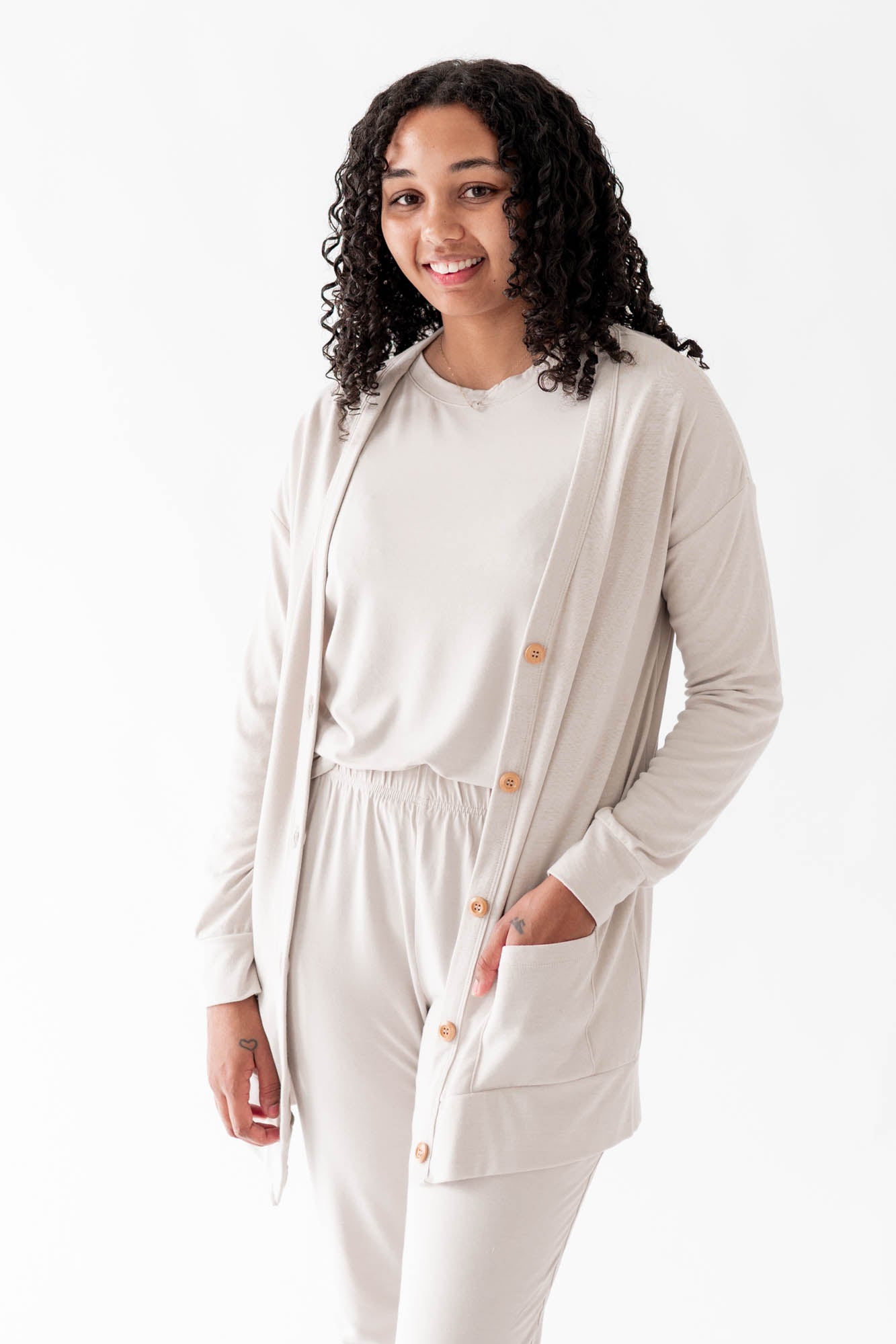 Model wearing the Bamboo Jersey Adult Cardigan in Oat overtop an Oat shirt and Oat pants