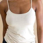 Woman wearing a beige spaghetti strap top and black pants against a beige background