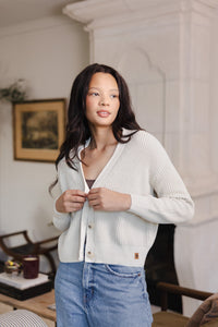 Woman looking over her shoulder buttoning her cropped cardigan in oat